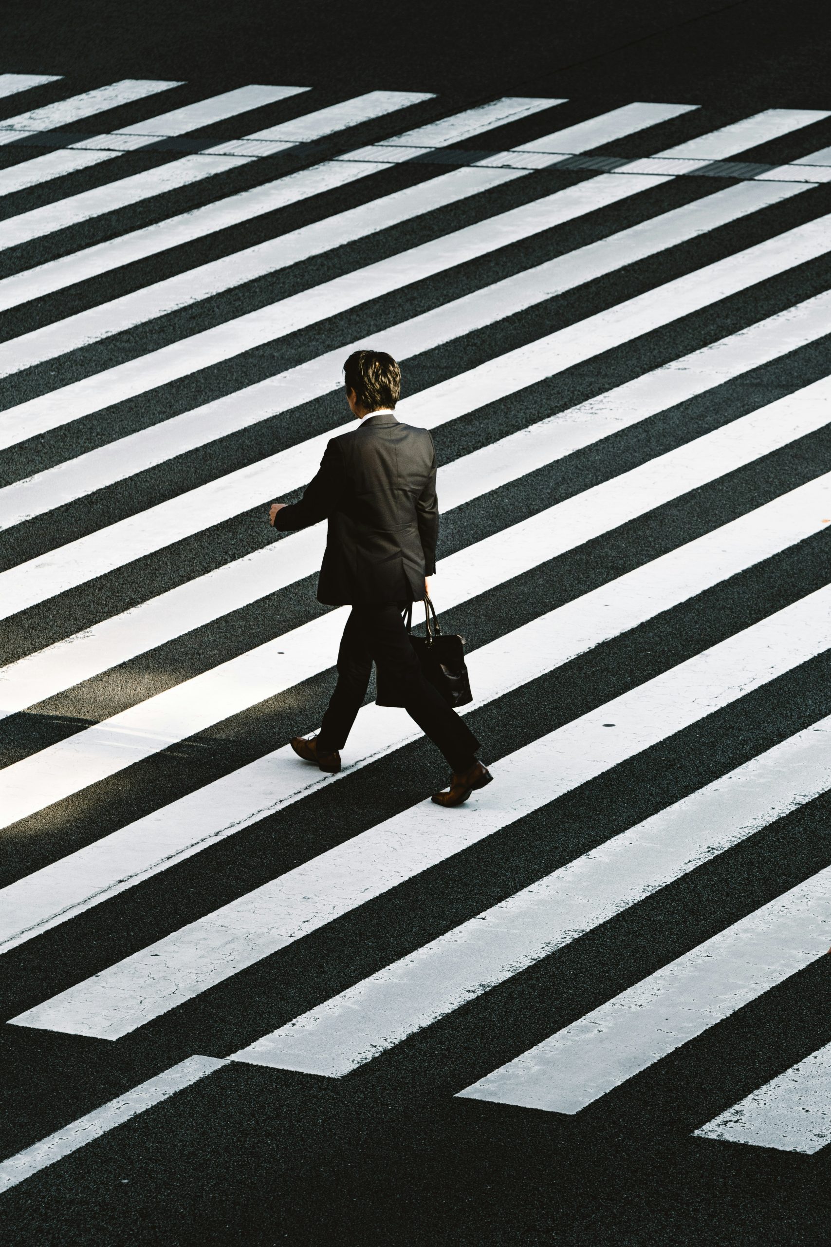 Man in dark suit walks across zebra crossing.